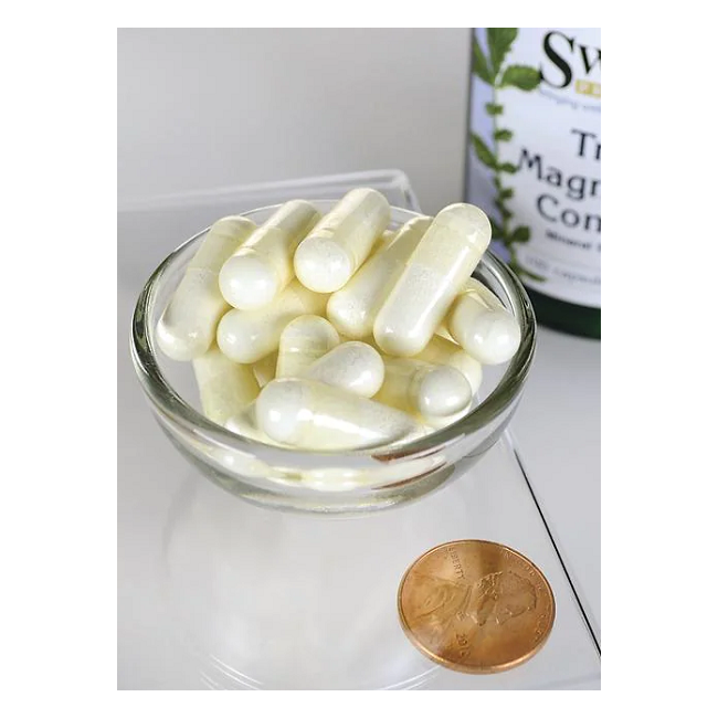 A bowl of white capsules is next to a penny for size reference, with a bottle labeled "Triple Magnesium Complex 400 mg" by Swanson partially visible in the background, highlighting its role as a magnesium supplement for bone and muscle support.