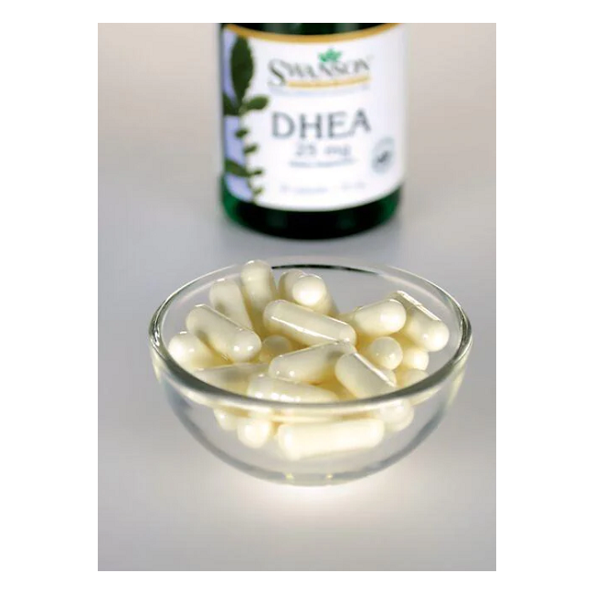 A small glass bowl filled with white capsules is in the foreground, while a blurred bottle labeled "Swanson DHEA 25 mg 30 Capsules - High Potency" in the background suggests support for hormonal balance and energy levels.