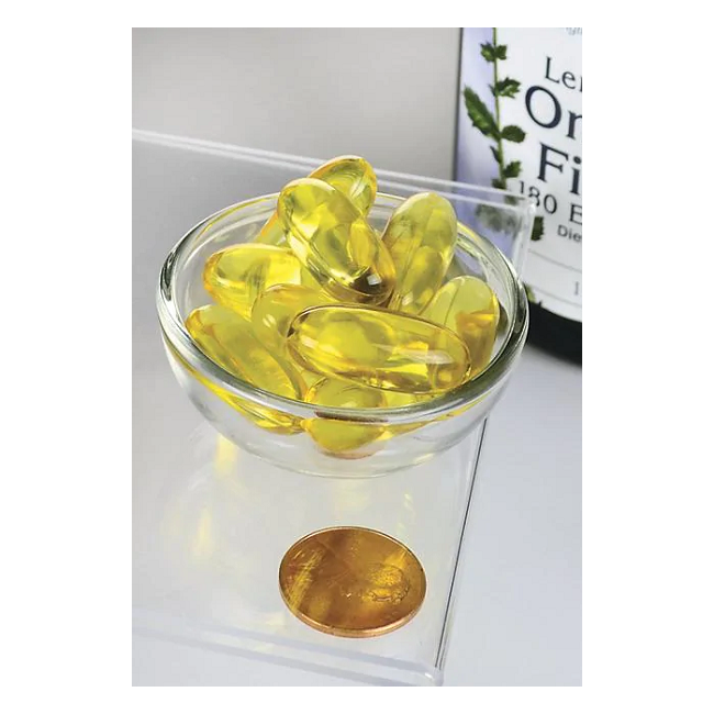 A small glass bowl holds yellow capsules next to a penny and a bottle labeled "Swanson Omega-3 Fish Oil - Lemon Flavour 150 Softgels" on a clear surface.