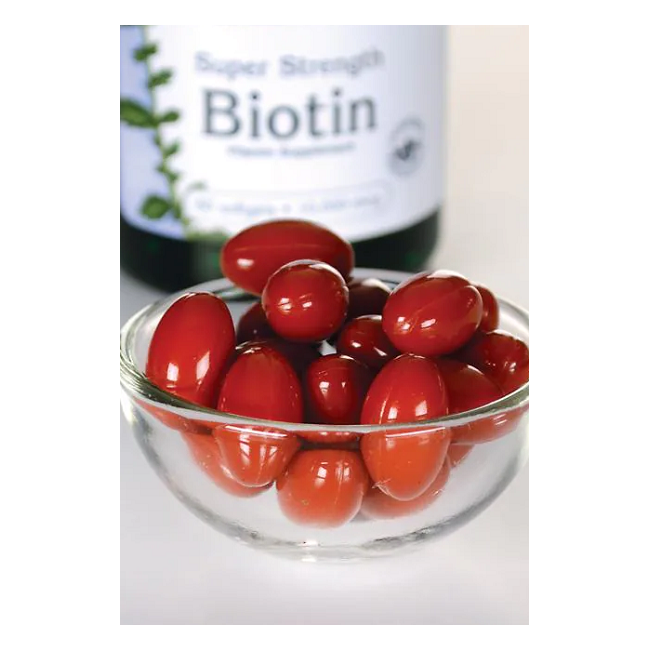 A glass bowl of small red tomatoes sits in front of a Swanson bottle labeled "Biotin - 10000 mcg 60 softgel," promising benefits for vibrant skin and luscious hair.