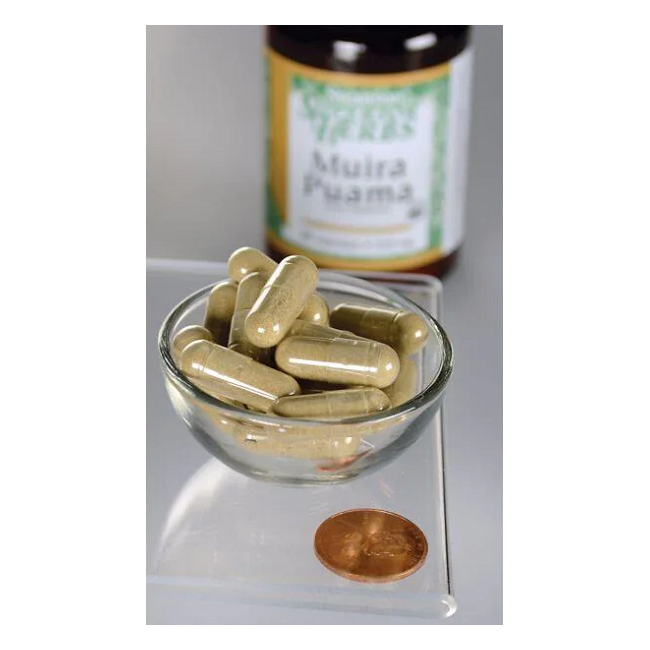 A small glass bowl with beige capsules sits beside a penny, suggesting the potent benefits of Swanson's Muira Puama - 10:1 Root Extract for sexual health. A blurred bottle labeled "Muira Puama" in the background adds a mysterious touch to this natural aphrodisiac.