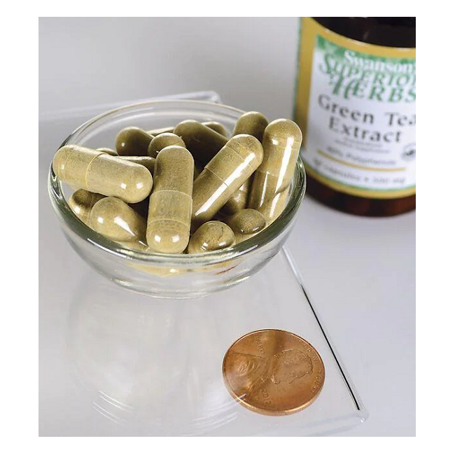 A bowl of green capsules, rich in polyphenols and antioxidants, sits next to a U.S. penny for scale, with a Swanson "Green Tea Extract 500 mg 60 Capsules" bottle in the background.