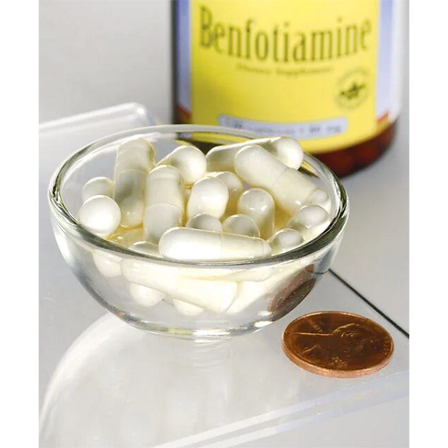 A glass bowl filled with white capsules is displayed next to a penny for size comparison, illustrating the dimensions of this dietary supplement. In the background, a partially visible bottle labeled "Swanson Benfotiamine (Vitamin B1) 80 mg 120 Capsules" features this thiamine derivative formulated to support overall health.