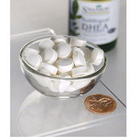 Vorschaubild für Eine Schale mit weißen Pillen neben einer Flasche Swanson DHEA - 25 mg 60 Lutschtabletten Kirschgeschmack.