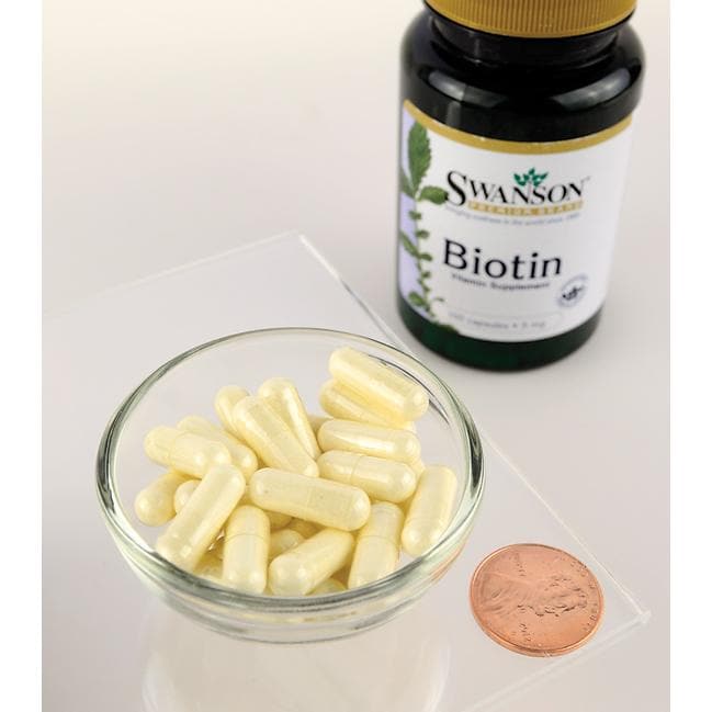 Eine Nahrungsergänzungsflasche mit Swanson Biotin - 5 mg 100 Kapseln neben einem Pfennig auf einem Tisch.