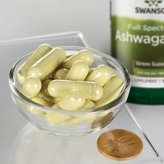 Eine Schale mit Swanson Ashwagandha - 450 mg 100 Kapseln mit einer Münze daneben.
