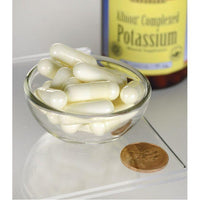 Thumbnail for A glass bowl filled with Swanson Albion Chelated Potassium Glycinate 99 mg 90 capsules next to a container of potassium supplement and a penny for scale.