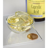 Vorschaubild für Swanson's Caprylsäure - 600 mg 60 Softgel Kapseln zur Nahrungsergänzung in einer Schale neben einer Münze.
