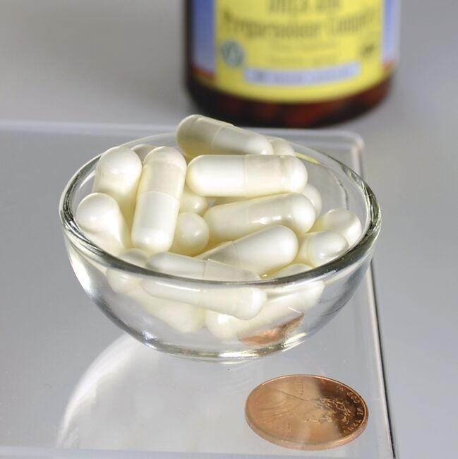 A bowl of white Swanson DHEA - 25 mg and Pregnenolone - 100 mg Complex 60 Veggie Capsules with a penny for scale and a blurred bottle in the background.